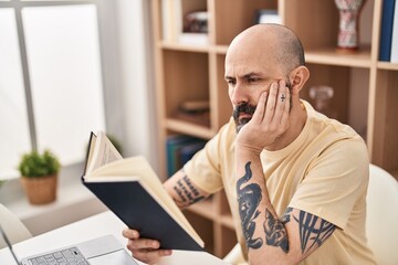 Young bald man reading book sitting on table at home