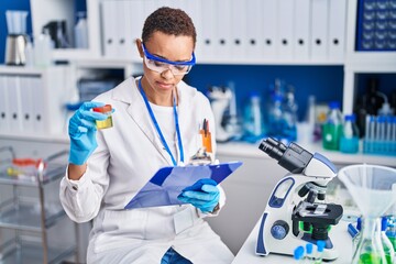 African american woman scientist holding urine test tube reading document at laboratory