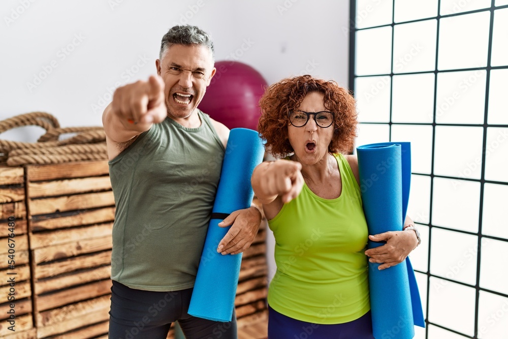 Sticker middle age couple holding yoga mat pointing displeased and frustrated to the camera, angry and furio