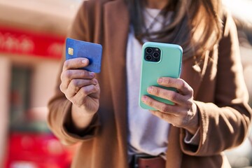 Young beautiful hispanic woman using smartphone and credit card at street