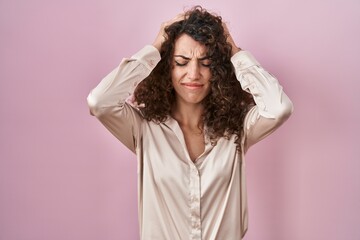 Naklejka premium Hispanic woman with curly hair standing over pink background suffering from headache desperate and stressed because pain and migraine. hands on head.