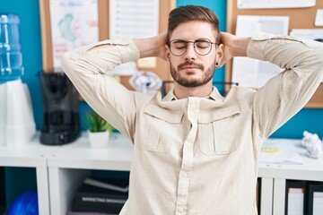 Young caucasian man business worker relaxed with hands on head at office