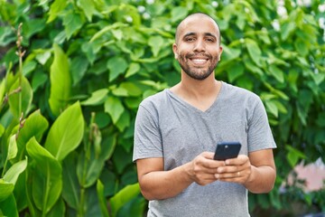 Naklejka na ściany i meble Young latin man smiling confident using smartphone at park
