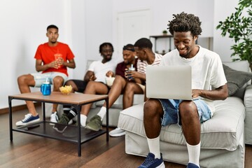 Group of african american people sitting on the sofa at home. Man smiling happy using laptop.