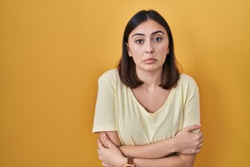 Obraz premium Hispanic girl wearing casual t shirt over yellow background shaking and freezing for winter cold with sad and shock expression on face