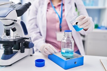 Fototapeta premium Young beautiful plus size woman scientist pouring liquid on test tube weighing liquid at laboratory