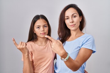 Young mother and daughter standing over white background pointing with hand finger to the side showing advertisement, serious and calm face