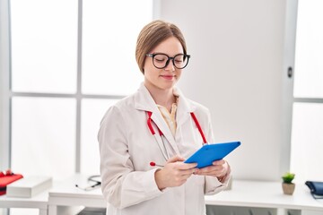 Young blonde woman wearing doctor uniform using touchpad at clinic