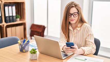 Young blonde woman business worker using laptop and smartphone at office