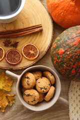Cup of tea or coffee, seasonal spices, bowl of cookies, blanket, pumpkins, colorful leaves, books and tangerines on wooden table. Cozy hygge at home. Top view.
