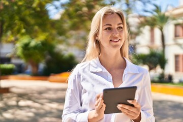 Young blonde woman smiling confident using touchpad at park