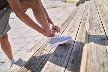 Middle age hispanic man tying shoe at street