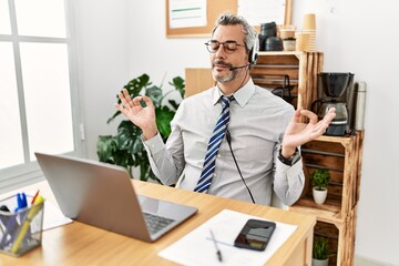 Middle age hispanic business man working at the office wearing operator headset relax and smiling with eyes closed doing meditation gesture with fingers. yoga concept.