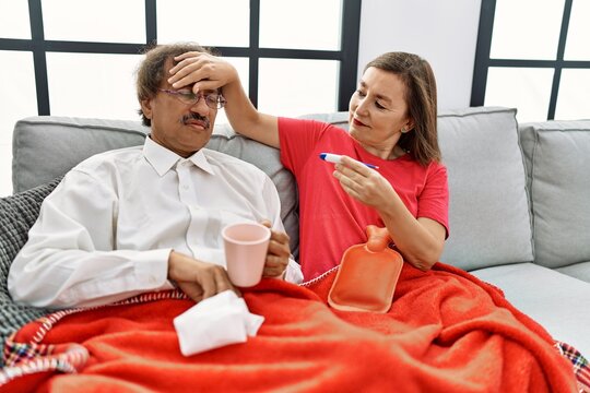 Middle age man and woman couple illness using thermometer sitting on the sofa at home