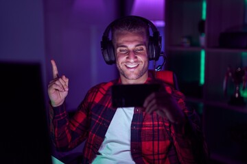 Young caucasian man playing video games with smartphone smiling happy pointing with hand and finger to the side