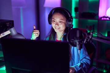 Young asian woman playing video games smiling happy and positive, thumb up doing excellent and approval sign
