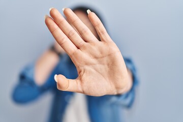 Obraz premium Hispanic woman standing over blue background covering eyes with hands and doing stop gesture with sad and fear expression. embarrassed and negative concept.