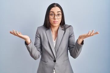 Hispanic business woman wearing glasses clueless and confused expression with arms and hands...