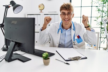 Young caucasian doctor man working at the clinic celebrating surprised and amazed for success with arms raised and open eyes. winner concept.