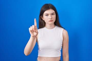 Young caucasian woman standing over blue background pointing with finger up and angry expression, showing no gesture