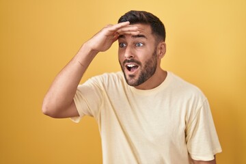 Handsome hispanic man standing over yellow background very happy and smiling looking far away with...