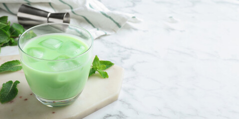 Delicious mint liqueur with ice cubes and green leaves on white marble table, closeup with space for text. Banner design