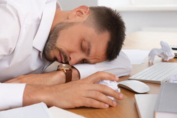 Fototapeta na wymiar Tired man sleeping at workplace in office