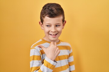 Young caucasian kid standing over yellow background smiling with happy face looking and pointing to...