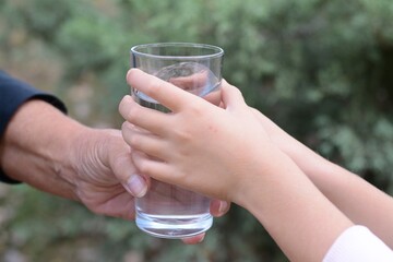 Child giving glass of water to elderly woman outdoors, closeup - obrazy, fototapety, plakaty