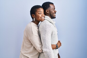 Young african american couple standing over blue background together looking to side, relax profile pose with natural face and confident smile. - Powered by Adobe