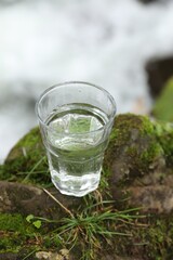 Glass of fresh water on stone with moss near stream, above view