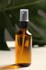 Spray bottle with oil and green leaf on white table. Natural cosmetics