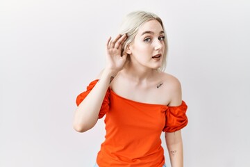 Young caucasian woman standing over isolated background smiling with hand over ear listening an hearing to rumor or gossip. deafness concept.