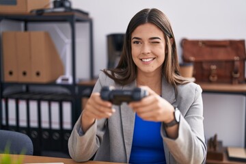 Hispanic woman working at the office playing video games winking looking at the camera with sexy...