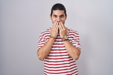 Hispanic man with long hair standing over isolated background laughing and embarrassed giggle...