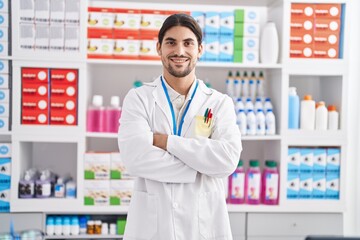 Young hispanic man pharmacist smiling confident standing with arms crossed gesture at pharmacy