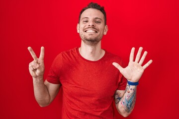 Young hispanic man standing over red background showing and pointing up with fingers number seven while smiling confident and happy.