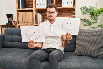 Young hispanic man working on depression holding sad to happy emotion paper skeptic and nervous,...
