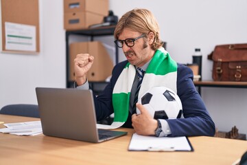Caucasian man with mustache working at the office supporting football team annoyed and frustrated...