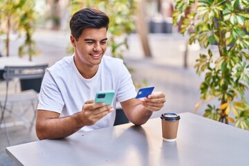 Young hispanic man using smartphone and credit card sitting on table at coffee shop terrace