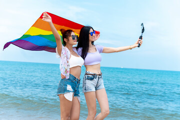 lesbian couple with LGBTQ flags on the beach, happy couple on vacation together at sea