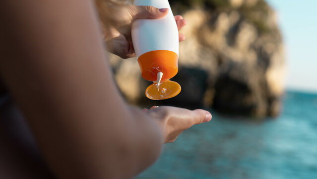 Woman's hand holding a bottle of sunscreen with the sea at the background. Antiaging, skin care, spf concept