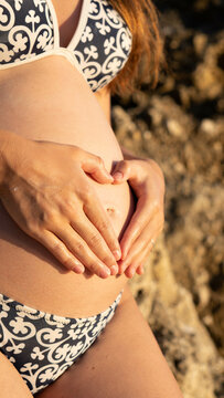 Close up picture of a pregnant woman in swimsuit holding her belly in the second trimester, showing love for the baby she carries