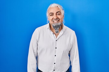 Middle age man with grey hair standing over blue background with a happy and cool smile on face. lucky person.