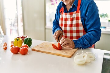 Senior man smiling confident cutting tomato at kitchen