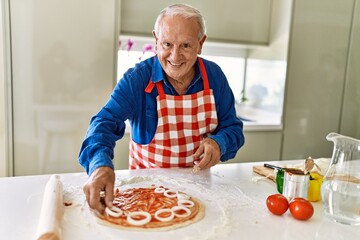 Senior man smiling confident cooking pizza at kitchen