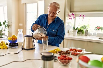 Senior man smiling confident pouring smoothie on glass at kitchen