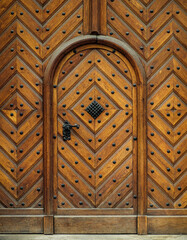 Old wooden door in medieval style with forged decor - rivets, a beautiful door handle and metal lattice on window. Arched entrance and wooden details of ancient building, exterior of Prague old city.