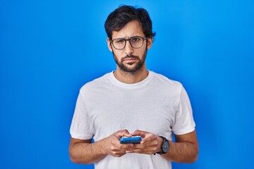 Handsome latin man using smartphone typing message skeptic and nervous, frowning upset because of problem. negative person.