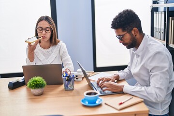 Man and woman business workers using laptop talking on smartphone at office